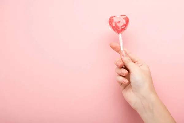 Vista ritagliata di donna che tiene a forma di cuore lecca-lecca su sfondo rosa — Foto stock