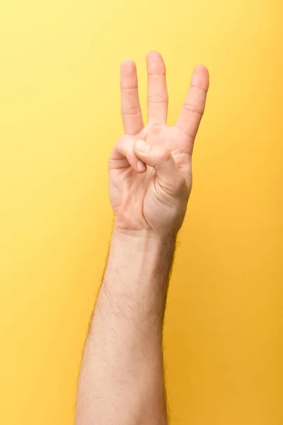 Обрезанный вид человека, показывающего три пальца на желтом фоне — стоковое фото