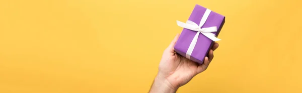 Panoramic shot of man holding gift on yellow background — Stock Photo