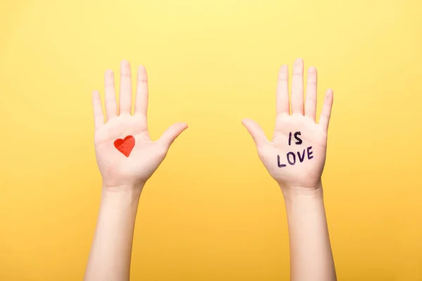 Vue recadrée de la femme montrant les paumes avec le cœur et est lettrage d'amour isolé sur jaune — Photo de stock