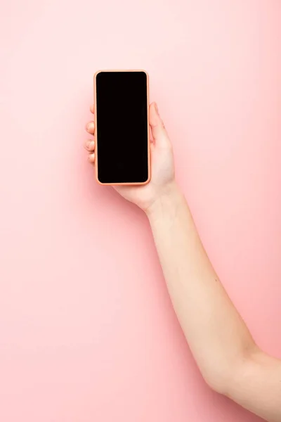 Vista recortada de la mujer sosteniendo teléfono inteligente sobre fondo rosa - foto de stock