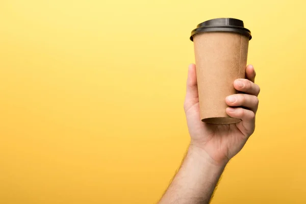 Cropped view of man holding paper cup on yellow background — Stock Photo
