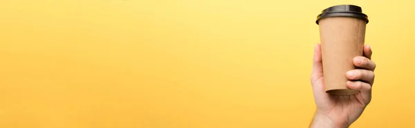 Панорамный снимок человека, держащего бумажную чашку на желтом фоне — стоковое фото
