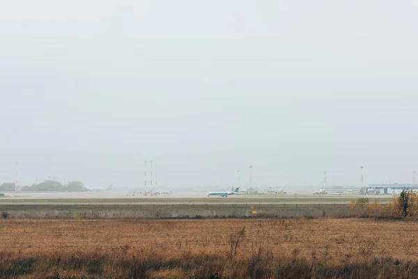 Campo de aviación cubierto de hierba con avión en pista y cielo nublado - foto de stock