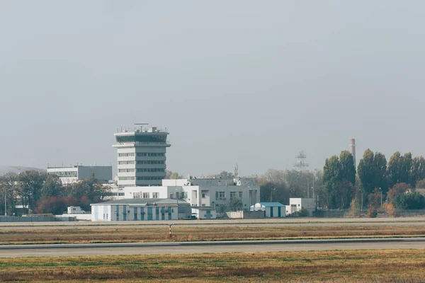 Runway on airfield with airport buildings at background — Stock Photo