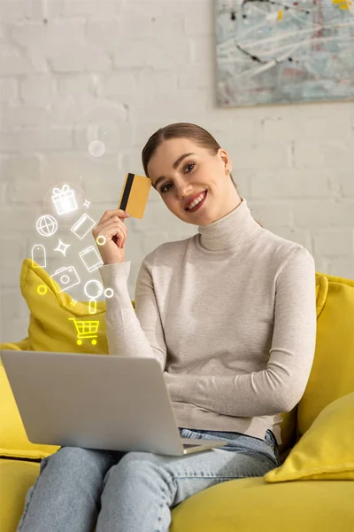 Souriante fille avec carte de crédit et ordinateur portable regardant la caméra près de l'illustration — Photo de stock