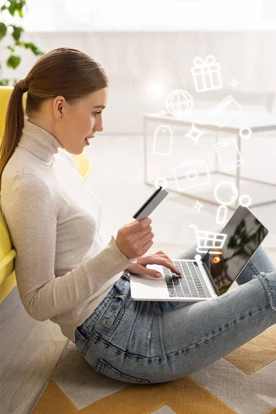 Vista lateral de la hermosa mujer con tarjeta de crédito y el uso de la computadora portátil cerca de la ilustración - foto de stock