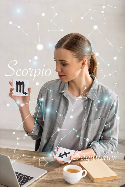 Астролог держит открытки со знаками зодиака рядом с книгой, ноутбуком и консолью — стоковое фото