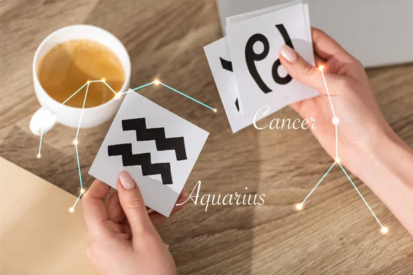 Vista recortada del astrólogo sosteniendo tarjetas con signos del zodíaco junto a constelaciones de cáncer y acuario - foto de stock