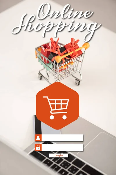 Ordenador portátil con tarjeta de crédito y regalos de juguete en el carrito en la mesa, concepto de compras en línea - foto de stock