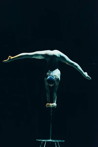 KYIV, UCRANIA - 1 DE NOVIEMBRE DE 2019: Vista posterior del acróbata balanceándose en las manos y haciendo split en circo aislado sobre negro - foto de stock