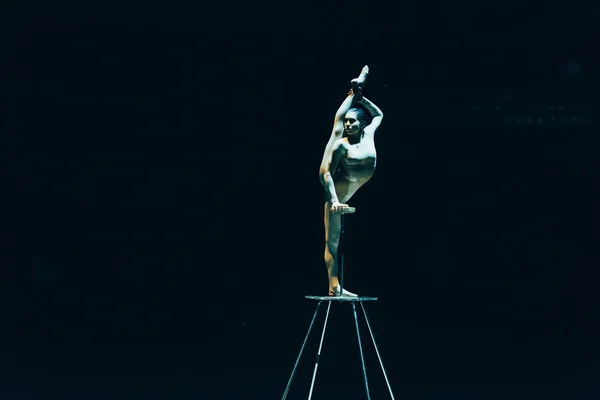 KYIV, UKRAINE - NOVEMBER 1, 2019: Flexible gymnast doing split while standing on equipment in circus isolated on black — Stock Photo