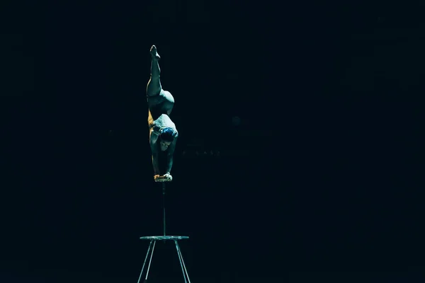 KYIV, UKRAINE - NOVEMBER 1, 2019: Back view of flexible acrobat balancing on hands in circus isolated on black — Stock Photo