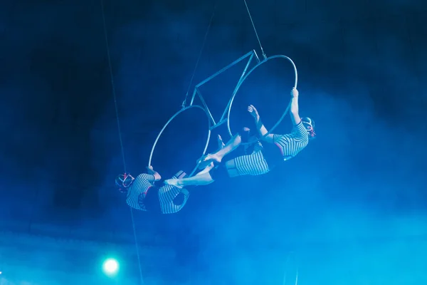 KYIV, UKRAINE - NOVEMBER 1, 2019: Low angle view of air gymnasts in smoke performing with rings in circus — Stock Photo