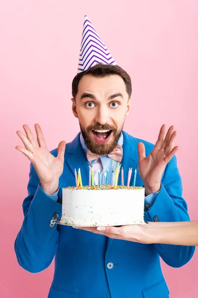 Vista recortada de la mujer de negocios celebración de pastel de cumpleaños cerca de empresario emocionado aislado en rosa - foto de stock
