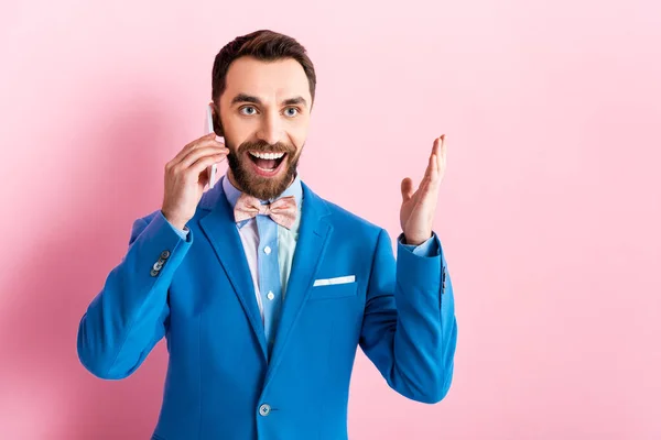 Hombre de negocios emocionado hablando en el teléfono inteligente y el gesto en rosa - foto de stock