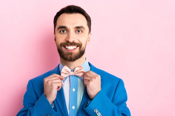 Feliz barbudo hombre de negocios tocando pajarita en rosa - foto de stock