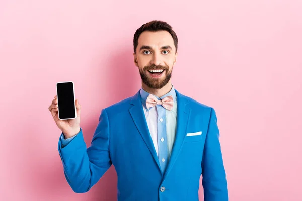 Happy bearded businessman holding smartphone with blank screen on pink — Stock Photo