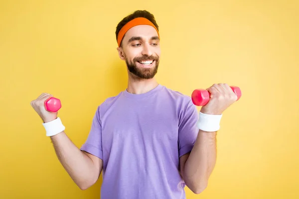 Cheerful sportsman exercising with small dumbbells isolated on yellow — Stock Photo