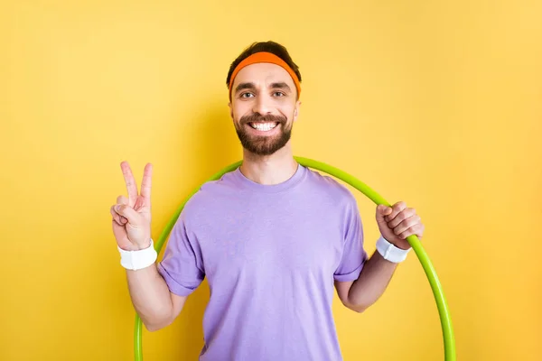Веселый спортсмен показывает знак мира и держит обруч хула на желтом — стоковое фото