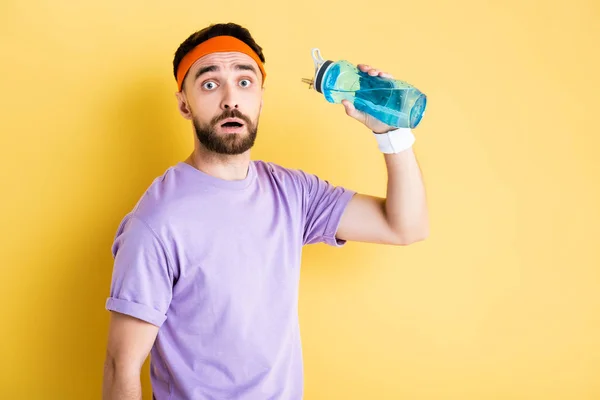 Preoccupato sportivo in possesso di bottiglia sportiva con acqua su giallo — Foto stock