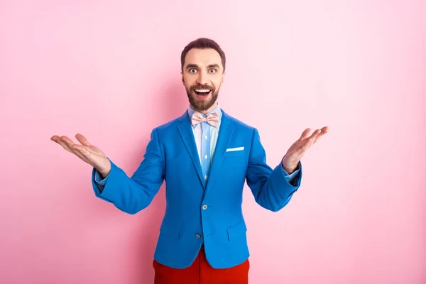 Hombre de negocios emocionado con las manos extendidas mirando a la cámara en rosa - foto de stock