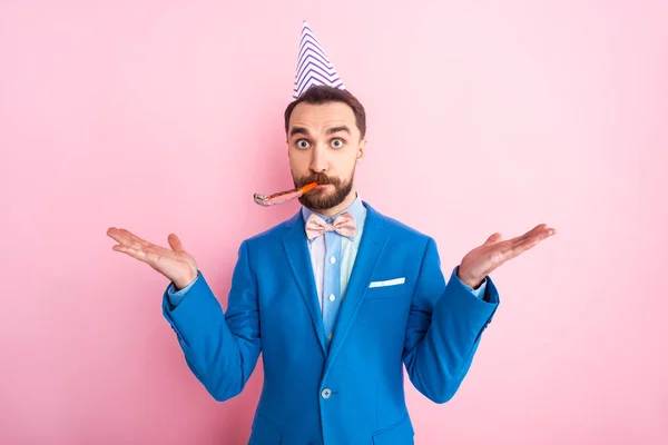 Confused businessman in party cap showing shrug gesture isolated on pink — Stock Photo