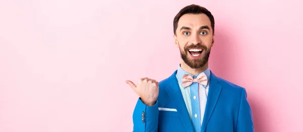 Panoramic shot of happy businessman pointing with finger on pink — Stock Photo