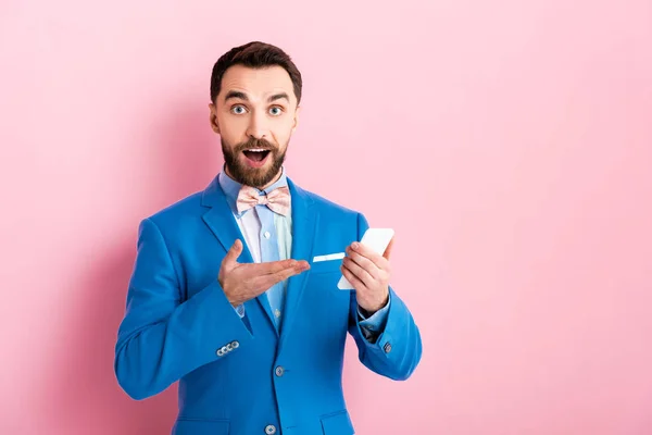 Surprised businessman pointing with hand at smartphone on pink — Stock Photo