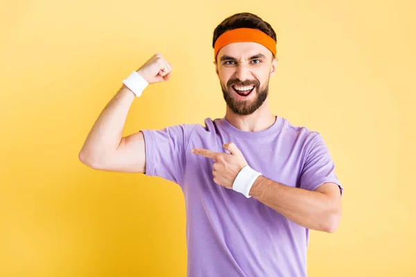 Hombre excitado apuntando con el dedo al músculo aislado en amarillo - foto de stock