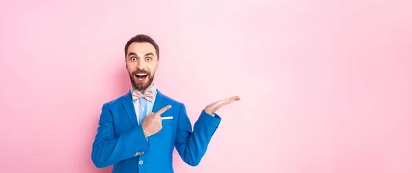 Hombre excitado tiro panorámico en traje señalando con el dedo en rosa - foto de stock