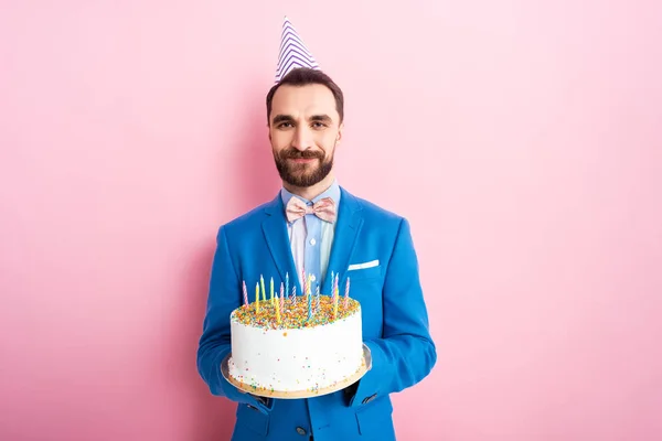 Cheerful bearded man in suit holding birthday cake on pink — Stock Photo