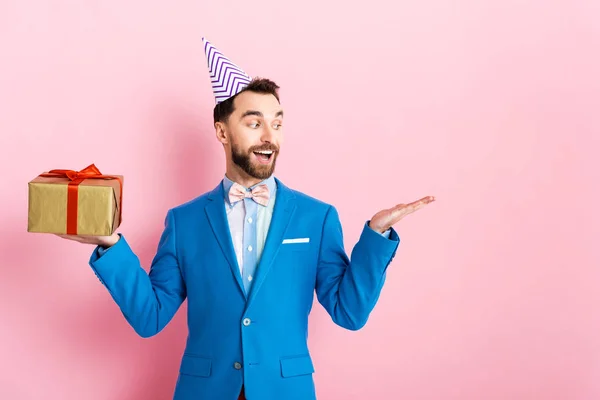 Homem de negócios feliz segurando presente e apontando com a mão em rosa — Fotografia de Stock