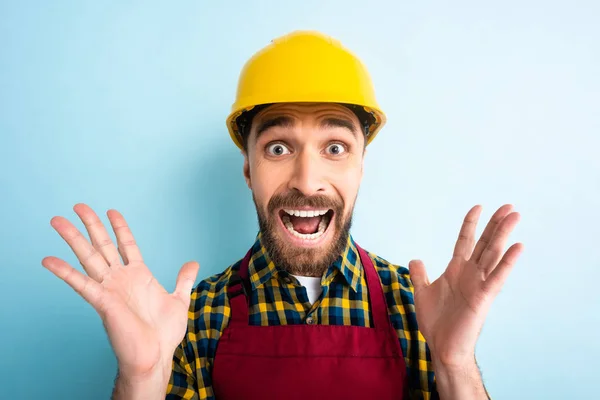 Trabajador asustado en casco de seguridad mirando a la cámara mientras grita en azul — Stock Photo