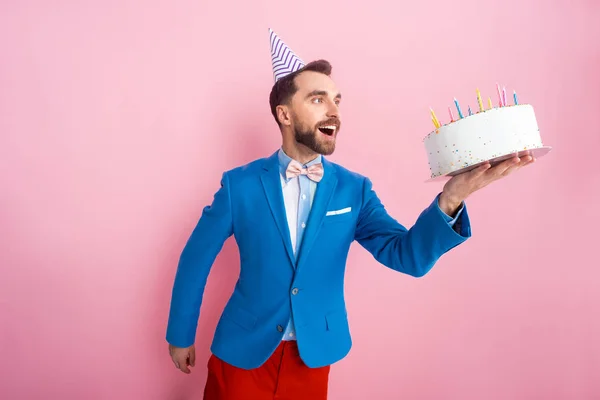 Positive businessman in suit looking at birthday cake on pink — Stock Photo