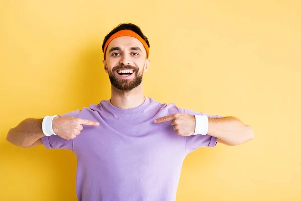 Glücklicher Sportler mit Stirnband, der mit den Fingern auf gelb zeigt — Stockfoto