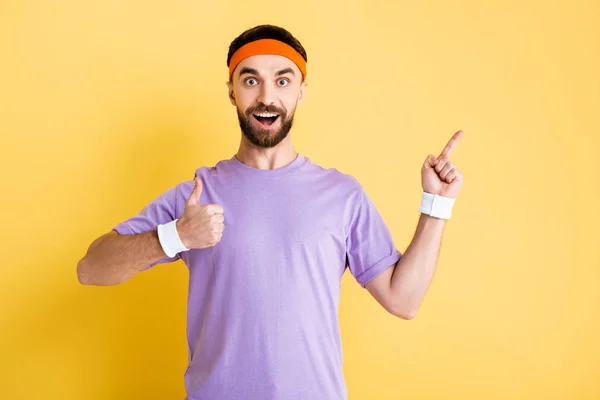 Happy sportsman pointing with finger and showing thumb up isolated on yellow — Stock Photo