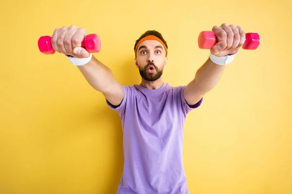 Selective focus of bearded sportsman exercising with small pink dumbbells on yellow — Stock Photo