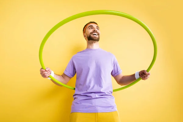 Low angle view of cheerful sportsman exercising with hula hoop on yellow — Stock Photo