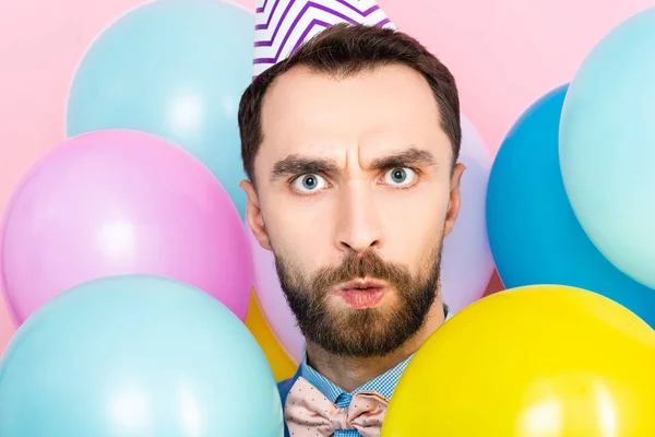 Surprised bearded man looking at camera near balloons isolated on pink — Stock Photo