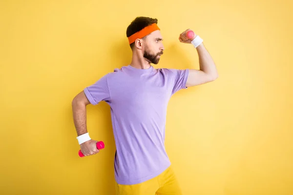 Vue latérale du sportif travaillant avec des haltères roses sur jaune — Photo de stock