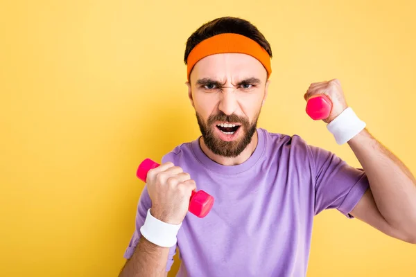 Emotional sportsman working out with small dumbbells isolated on yellow — Stock Photo