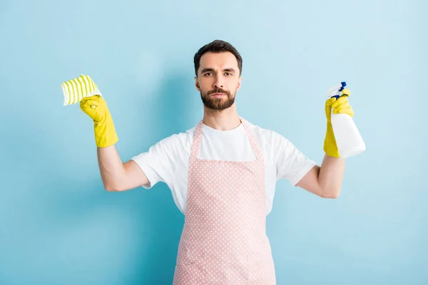 Homem barbudo segurando pano e spray garrafa para limpeza em azul — Fotografia de Stock