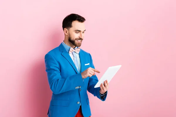 Hombre barbudo alegre apuntando con el dedo a la tableta digital en rosa - foto de stock