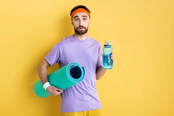 Bärtiger Mann mit Sportflasche und Fitnessmatte auf gelb — Stockfoto