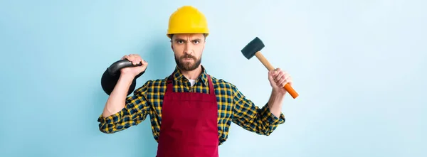 Panoramaaufnahme eines wütenden Arbeiters mit Hammer und Hantel auf blauem Grund — Stockfoto