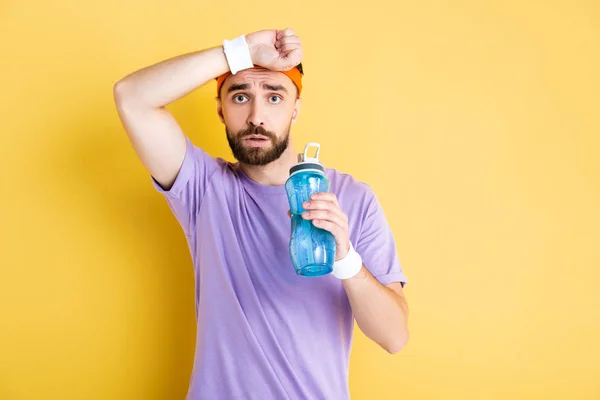 Sportif fatigué tenant bouteille de sport sur jaune — Photo de stock