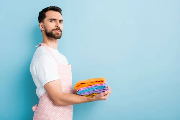 Schöner bärtiger Mann in Schürze mit sauberer Kleidung auf blauem Grund — Stockfoto