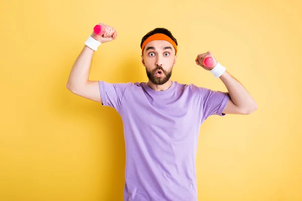 Schockierter Sportler mit Stirnband trainiert mit kleinen Hanteln auf gelb — Stockfoto