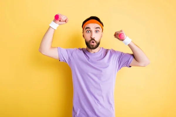 Sportivo scioccato in fascia che si allena con piccoli manubri su giallo — Foto stock